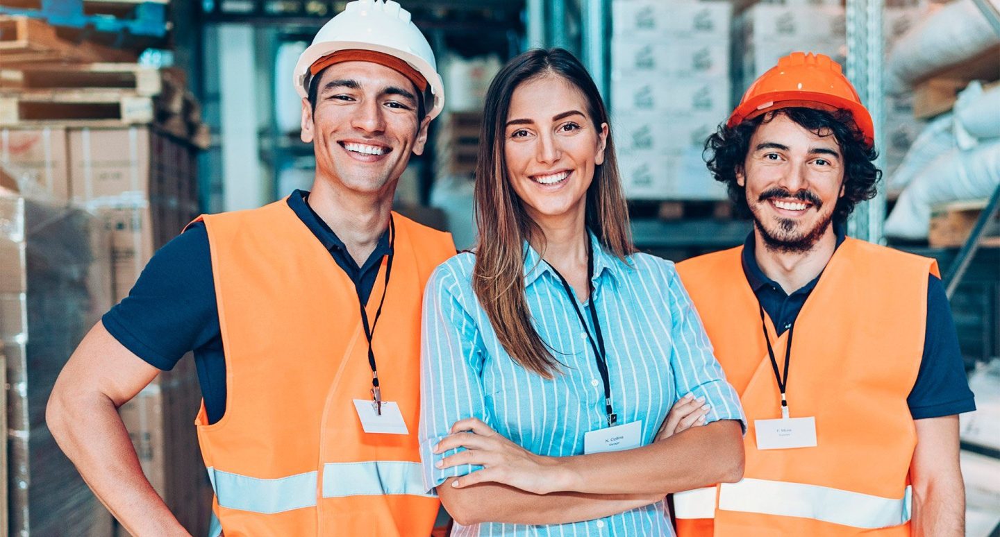 Three workers smiling in an industrial warehouse.