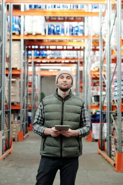 Man standing in warehouse, using tablet for inventory management.