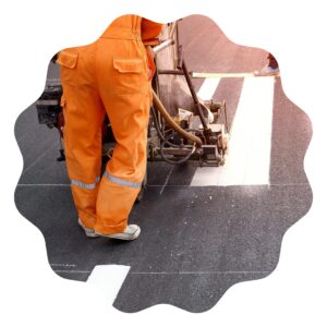 a roadline operator wearing a hi vis orange uniform is painting a pedestrian crossing on a road