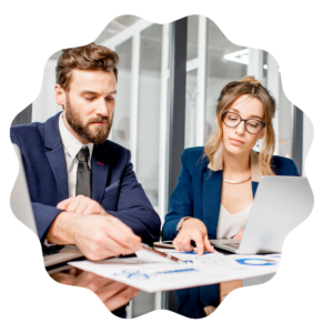 A man and woman in business attire sitting at a table with a laptop discussing marketing analytics and business management processes